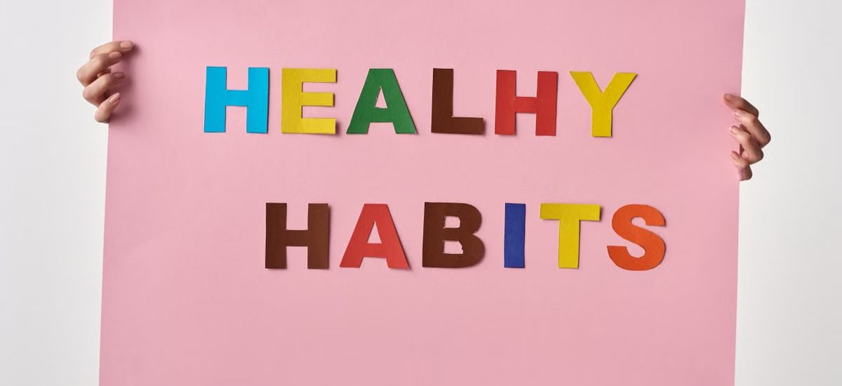 A woman holds a pink poster with colorful letters spelling 'HEALTHY HABITS'.